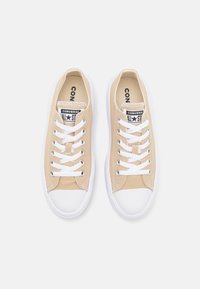 Beige canvas sneakers met witte rubberen zolen en veters. Voorzien van een zwart-wit logo patch op de tong. Klassiek laag ontwerp.