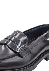 Mocassino in pelle nera con finitura lucida, caratterizzato da un accento cucito sulla tomaia e una suola in gomma testurizzata.