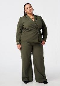 Olijfgroene twee-delige kostuum met een wikkelstijl blazer, wijde broek en een strik taille. Kenmerkt zich door gladde stof en subtiele glans.