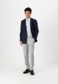 Navy double-breasted blazer, light blue striped shirt, light gray tailored pants, black shoes; fitted, smooth fabric with no visible patterns.