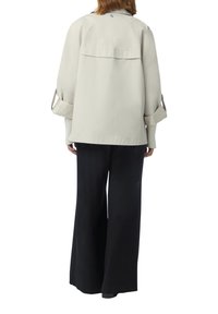 Veste surdimensionnée gris clair avec un empiècement au dos et des poignets retroussés, assortie à un pantalon large noir. Tissu lisse, design simple, détails minimalistes.