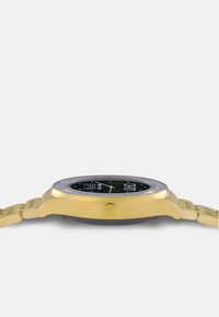 Orologio dorato con cassa rotonda, quadrante nero, marcatori delle ore bianchi e un cinturino giallo testurizzato. Presenta una corona di lato.