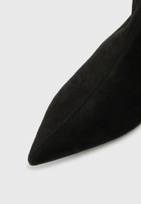 Špicat nosek črne semiš gležnjarice s vidno šivanjem na belem ozadju.