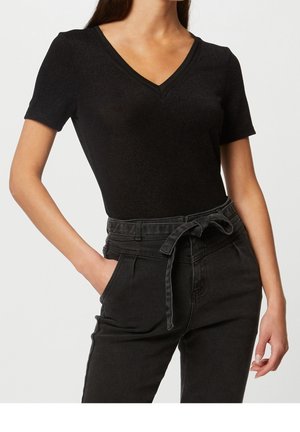 Vrouw draagt een aansluitend zwart V-hals T-shirt met korte mouwen, ingestopt in een hooggetailleerde zwarte broek met een gebonden stoffen riem.