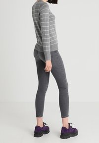Grau gestreifter langärmeliger Pullover, eng anliegende graue Jeans und klobige lila Sneakers. Glattes Material mit gerippten Bündchen und Säumen.