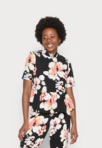 Top peplum floral com fundo preto, grandes flores brancas e rosas, mangas curtas e colarinho com babados. Combinado com calças correspondentes.