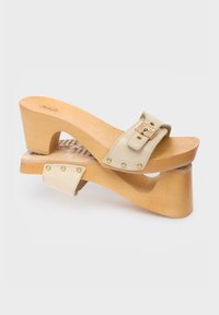 Beige leather heeled sandals with a wooden platform, featuring a wide strap, gold buckle, and decorative studs along the edges.