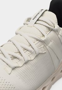 Κοντινό πλάνο λευκού αθλητικού παπουτσιού μάρκας Columbia με υφασμάτινο δίχτυ και πολλαπλά κορδόνια σε ανοιχτόχρωμη σόλα.