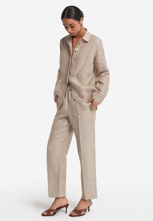 Linne skjorta och byxor i ljusbeige. Skjortan har spetsig krage och knappar; byxorna är strukturerade med rak ben och elastisk midja.