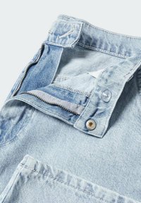 Zone de la taille d'un jean en denim bleu clair avec fermeture éclair ouverte, bouton et boutonnière visibles sur fond blanc.