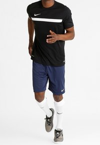 Nike activewear set includes a black short-sleeve shirt with a white stripe, blue shorts, white socks, and gray athletic shoes.