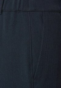 Tmavě modré kalhoty s vzorem rybí kosti, s hladkou texturou a boční kapsou. Jednoduchý design pasu, bez viditelných zapínání.