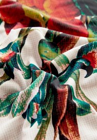 Colorful floral fabric with vibrant red, green, and black patterns, featuring a smooth texture and soft drape.