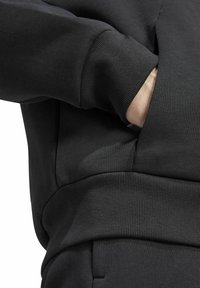 Felpa nera con polsini a coste, design a tasca e texture liscia, con un focus su una vestibilità rilassata e uno stile minimalista.