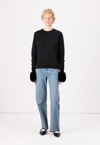 Zwarte sweatshirt met ribgebreide manchetten, gecombineerd met lichtblauwe rechtliggende jeans. De manchetten hebben zwarte bontaccenten en worden gedragen met zwarte schoenen.