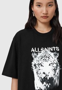 Camiseta de algodón negra con un gráfico de tigre blanco en estilo glitch y el texto "ALLSAINT'S" en la parte delantera. Diseño de manga corta y cuello redondo.