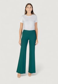 Pantaloni flare verdi con vita alta, abbinati a una t-shirt bianca a maniche corte. Tessuto morbido con un leggero luccichio.