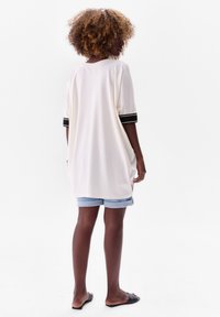 White oversized top with black striped sleeves, paired with light blue cuffed denim shorts. The fabric appears soft and relaxed.