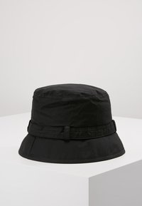 Chapeau seau noir en tissu doux avec un large bord descendant et une bande en tissu à la base. Texture lisse et design simple.