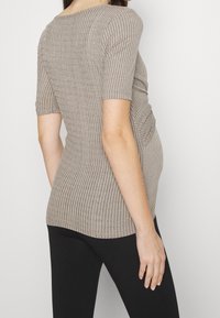 Beige ribbad stickad topp med korta ärmar, figurnära passform och sidsamlingdetalj. Matchas med svarta tajta leggings.