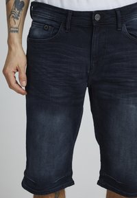 Shorts en denim bleu foncé avec une coupe slim, un design classique à cinq poches et un ourlet retroussé. Texture lisse avec de légers détails de décoloration.