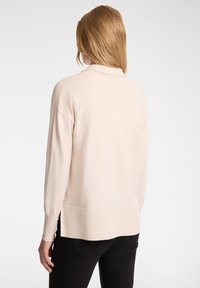 Maglione lavorato a maglia rosa chiaro con maniche lunghe, orlo a coste e vestibilità leggermente over size. Texture liscia, colletto arrotondato e spacco laterale.