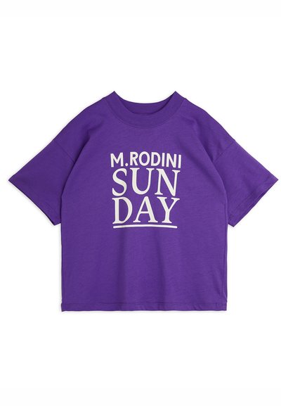 Camiseta de manga corta morada con un estampado gráfico blanco que dice "M. RODINI SUNDAY" centrado en el frente. Textura de tela suave.