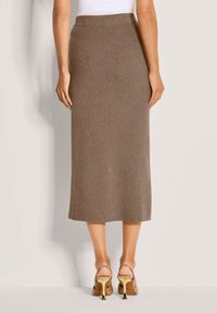 Gebreide, bruine maxi-rok met een hoge tailleband, zachte textuur en eenvoudig ontwerp, gecombineerd met strappy, lichtbruine hoge hakken.