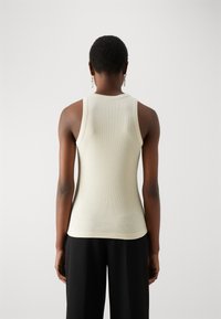 Top a maniche larghe in crema a costine con un design aderente, spalline larghe e scollatura rotonda, abbinato a pantaloni neri a gamba larga.