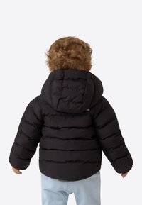 Czarna pikowana kurtka dla dziecka z kapturem, elastycznymi mankietami i poziomymi przeszyciami. Noszona na jasnoniebieskich spodniach. Miękka tekstura.