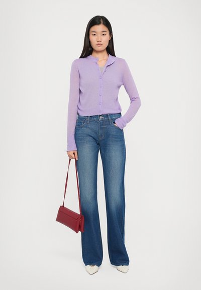 Lila knopenkaart, denim flared jeans, witte pointy schoenen en een rode schoudertas. De textuur lijkt zacht en de kleuren zijn levendig.