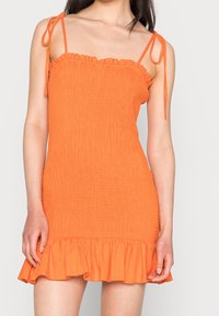 Oranžové, strukturované mini šaty s volánkovým lemem a nastavitelnými ramínky. Mají smockovanou sukni pro přiléhavý siluetu.