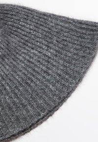 Tessuto in lana grigia a maglia, caratterizzato da una texture a coste, una finitura morbida e una forma curva simmetrica con accenti pelosi lungo i bordi.