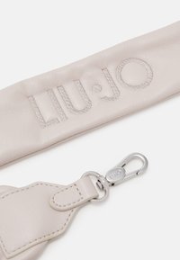 Bracelet en cuir beige avec "LIU·JO" brodé, doté d'une boucle argentée portant le même nom de marque sur fond blanc.