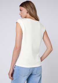 Top bianco a maniche corte realizzato in tessuto morbido, con una vestibilità comoda e scollo rotondo, abbinato a jeans blu chiaro.