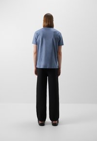 T-shirt azzurro chiaro a maniche corte con una superficie liscia, abbinato a pantaloni neri larghi. Le scarpe sono nere e leggermente lucide.