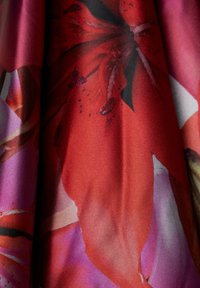 Barevná látka s velkými červenými květy a černými akcenty, hladký povrch a směs tmavě růžových a fialových odstínů.