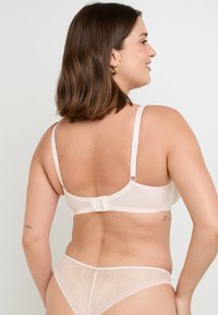 Reggiseno in pizzo nudo con un design testurizzato, spalline regolabili e chiusura a gancio sul retro. Abbinato a mutandine trasparenti coordinate.