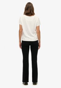 Witte T-shirt met korte mouwen en een ronde hals, gecombineerd met zwarte wijde jeans. De outfit heeft een strak, minimalistisch ontwerp.