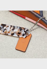 Lähenemine multivärvilise nahkhotelli nurgale, kus on kaks võtmehoidjatagi: üks kilpkonnamustriline ja teine oranž nahast, millel on pressitud logo.