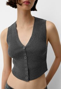 Grå ribbad stickad kort topp med djup V-ringning, med fem mörka knappar framtill och en figurnära design. Slät textur.