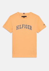 Πορτοκαλί βαμβακερό t-shirt με λογότυπο "HILFIGER" σε μπλε ναυτικό χρώμα κατά μήκος του στήθους, κοντά μανίκια και μικρό λογότυπο στη αριστερή πλευρά του μανικιού.