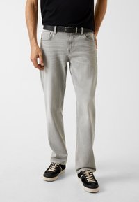 Lichtgrijze jeans met een losse pasvorm, vijf zakken en stikseldetails, gecombineerd met zwarte sneakers met een gestructureerde bovenkant en lichte veters.