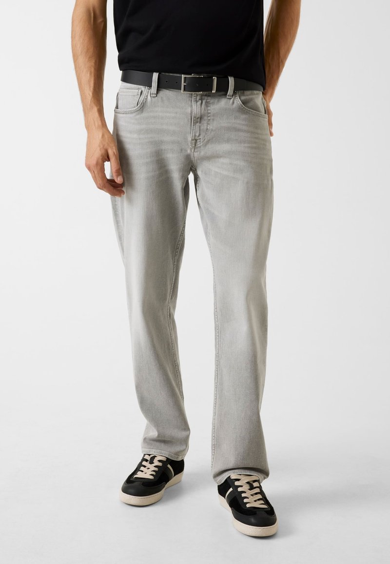 Lichtgrijze jeans met een losse pasvorm, vijf zakken en stikseldetails, gecombineerd met zwarte sneakers met een gestructureerde bovenkant en lichte veters.