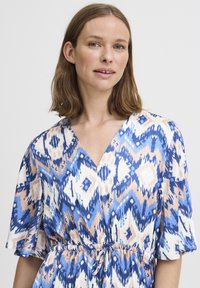 Robe à motifs bleus et roses avec un décolleté en V et de courtes manches flottantes, taille cintrée, fabriquée en tissu léger.