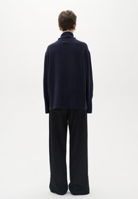 Tumši zila džemperis ar augsto apkakli, pārāk plaša piegriezuma un garām piedurknēm, apvienots ar brīviem melniem biksēm. Mīksta tekstūra un vienkāršs dizains.