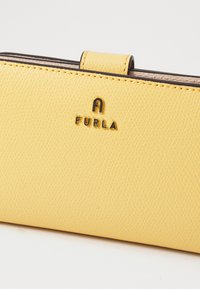 Portofel galben din piele cu o suprafață texturată, având un logo metalic Furla. Închidere sigură prin clichet și căptușeală interioară netedă.