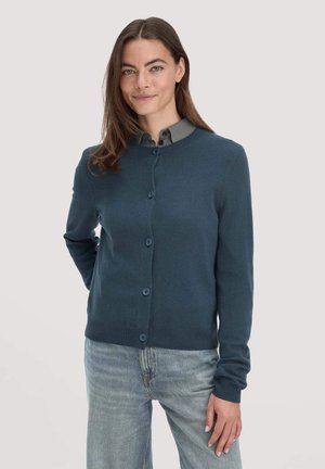 Navyblauwe cardigan, ronde halslijn, knopenfront, geribde manchetten en zoom, gemaakt van zacht materiaal, gedragen over een grijze overhemd met kraag.