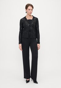 Czarny kardigan z cekinami i kołnierzykiem, zestawiony z dopasowanym czarnym topem oraz teksturowanymi szerokimi spodniami, noszony z czarnymi wysokimi obcasami.