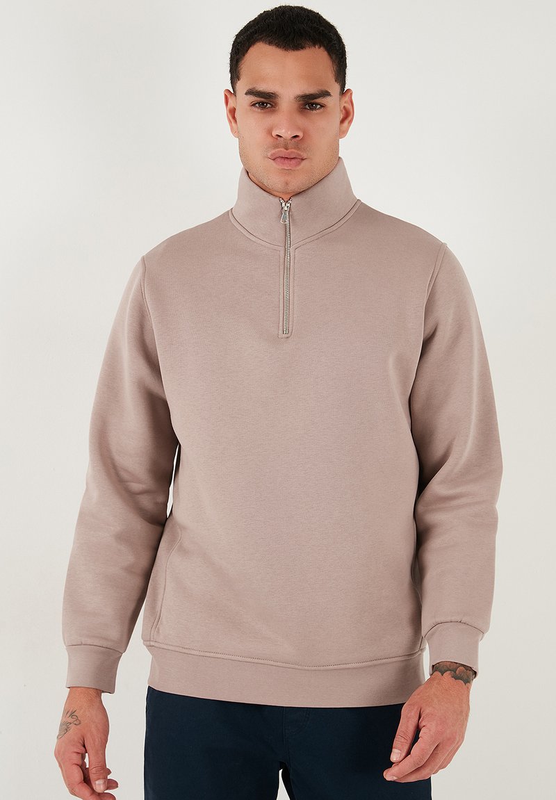 Sudadera de cremallera color beige claro con cuello alto, mangas largas, puños acanalados y un corte relajado. Textura suave y detalle de costura mínima.